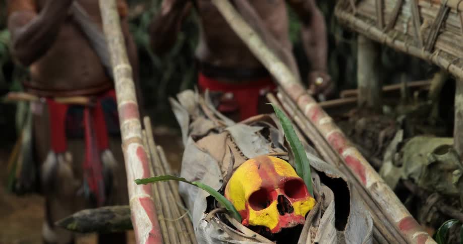 Tribal men showing a painted skull mounted on branches