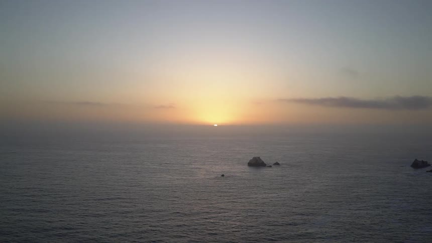 Ocean waves ripple as the sun sets in the distance
