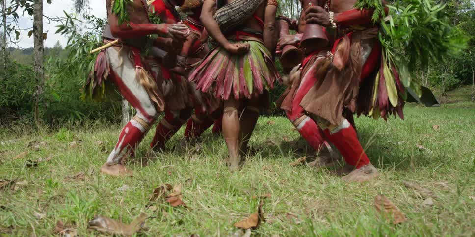 African men in full costume jump while performing some type of ceremony