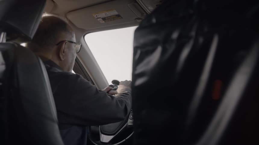 A man in glasses drives a car on a bumpy road