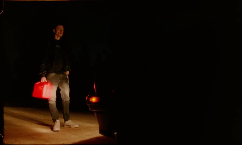 Man with a gas can standing in front of the headlamps of a car at night