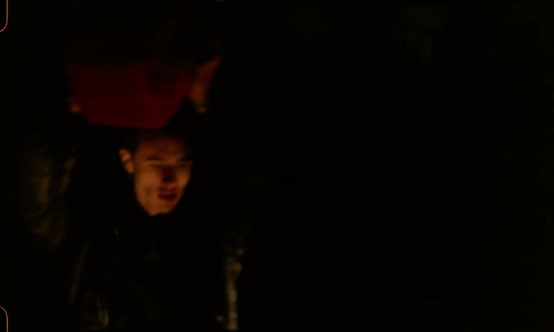 A man in a leather jacket and denim jeans pours fuel from a canister onto a vehicle at night