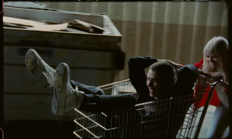 A young woman pushes a shopping cart with a young man inside it