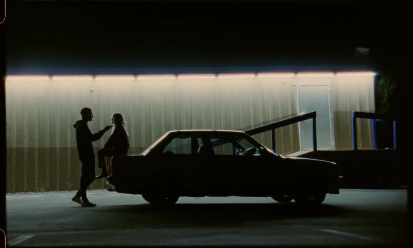 Woman sits on the back of a car with a man talking to her
