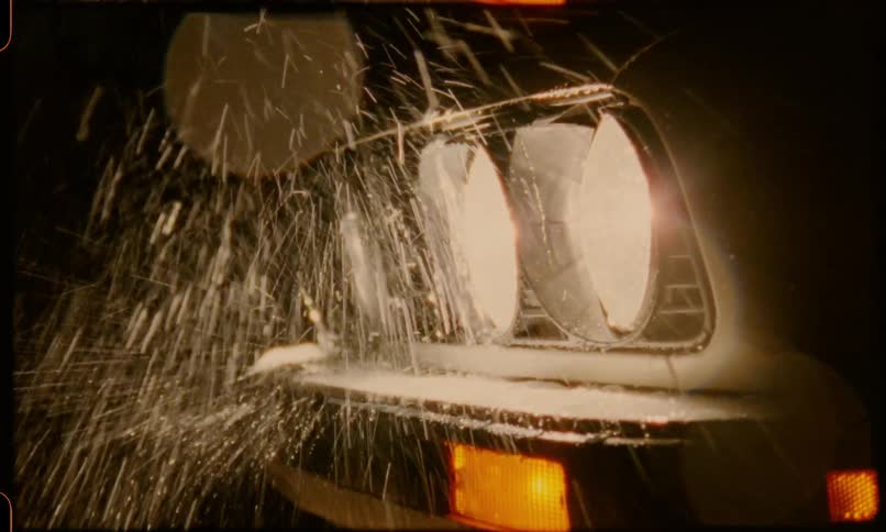 Water pours over the headlights of a car at night