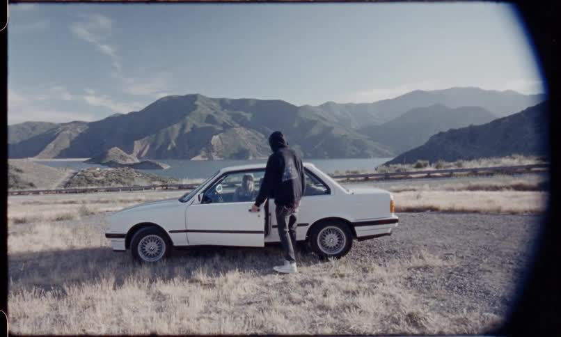 A man smokes a cigarette beside a car and then gets in the drivers seat