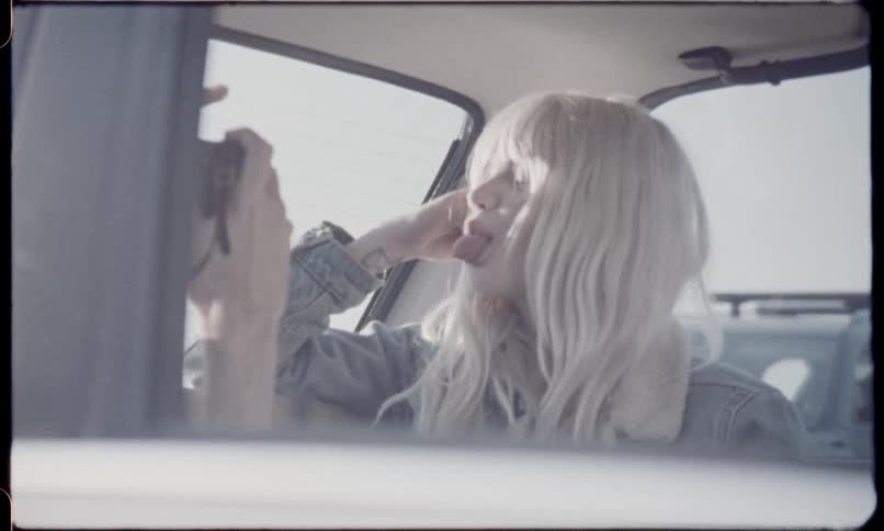 Blonde woman poses for the photographer and sticks out her tongue by smilingin the car on a sunny day