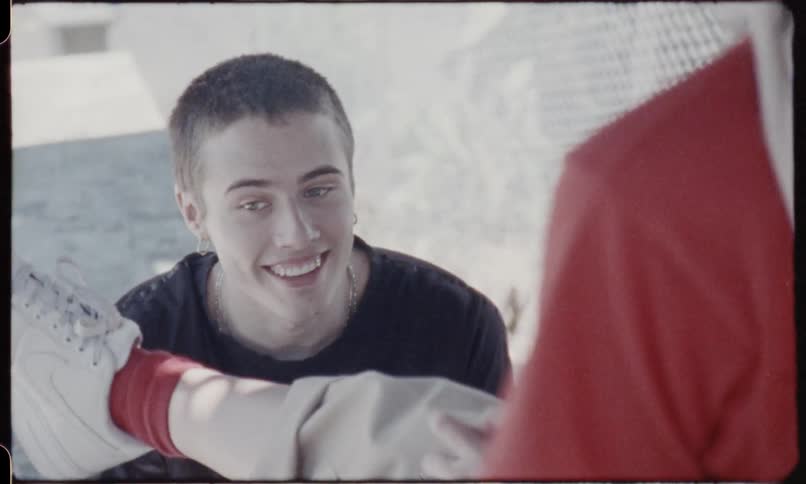 Boy wearing earrings and chain necklace looks up at girl and talk to her during daylight