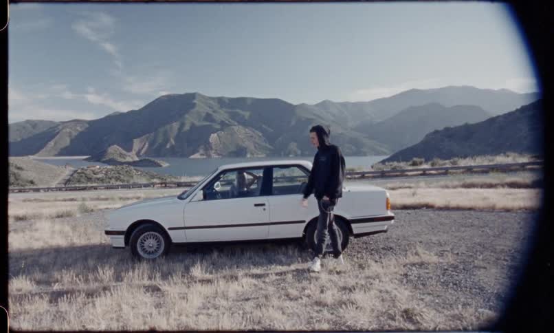 Man smoking a cigarette outside a car while a girl waits inside