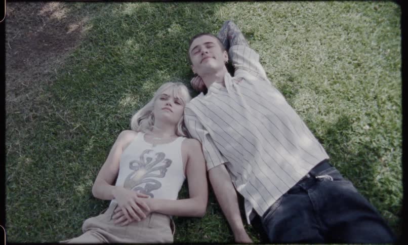 Man and blonde woman lie down on the grass under the shade of a tree during daylight