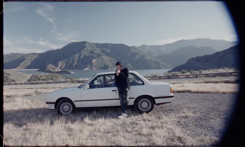Static shot of a person smoking while leaning on a car