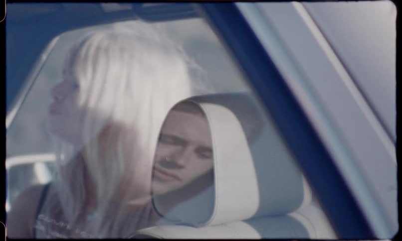 A man is smoking a cigarette outside of a vehicle that a woman is sitting in