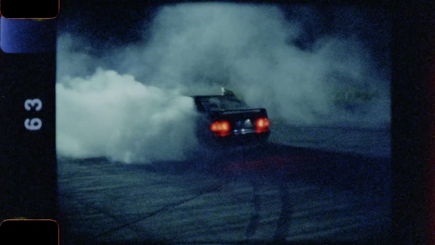Smoke billowing from a car sitting on a race course with its emergency lights blinking at night