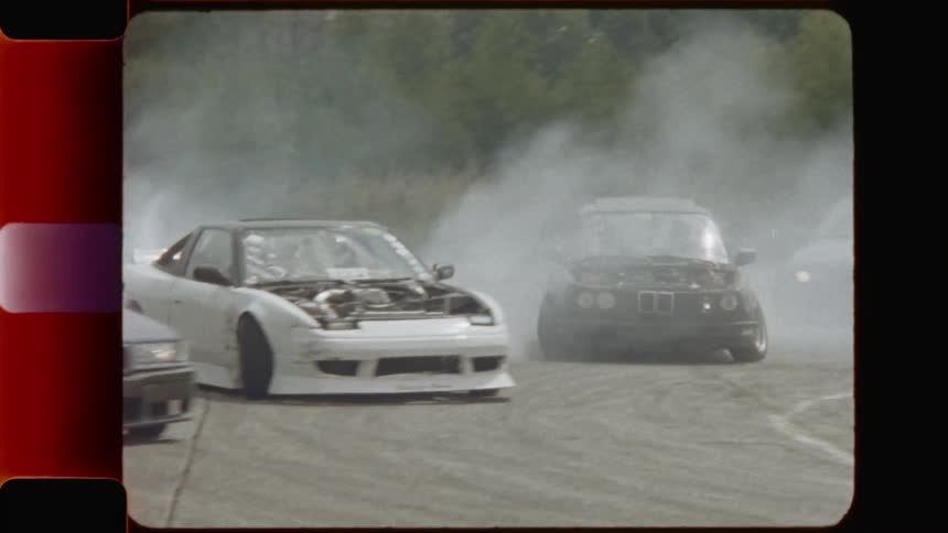 Race cars smoke while drifting around a corner on a race track
