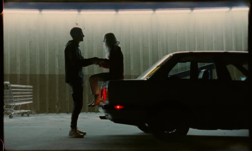 A couple playfully holding hands over the trunk of a car