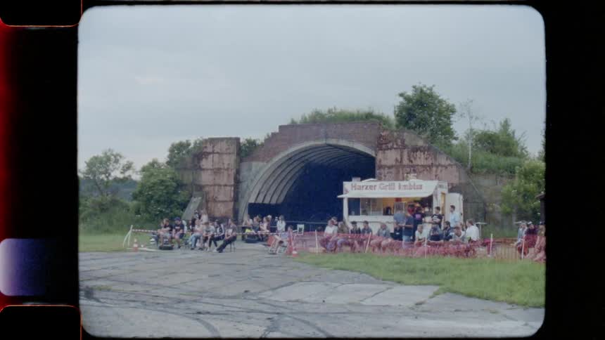 The camera looks at a group of people sitting next to a food vendor