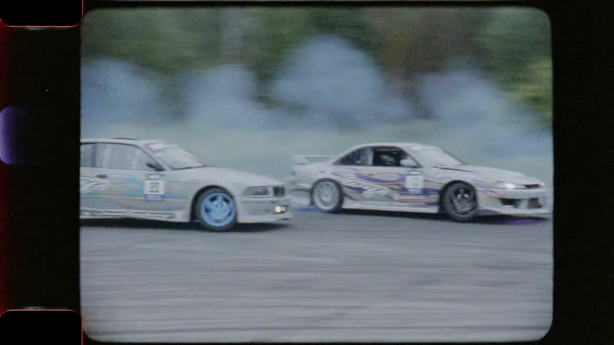 Cars race along track past woods and tents