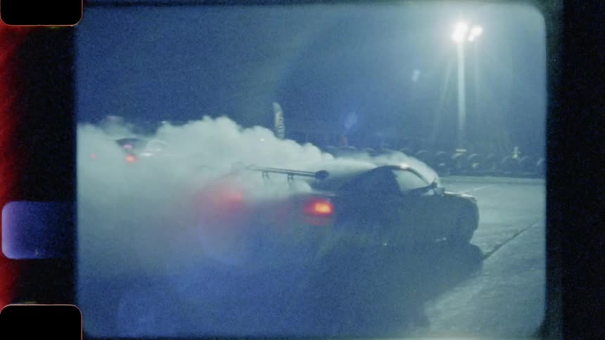 A car does a burnout at night under bright lights
