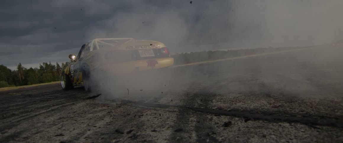 Yellow race car spins on the track and makes dust on a cloudy day