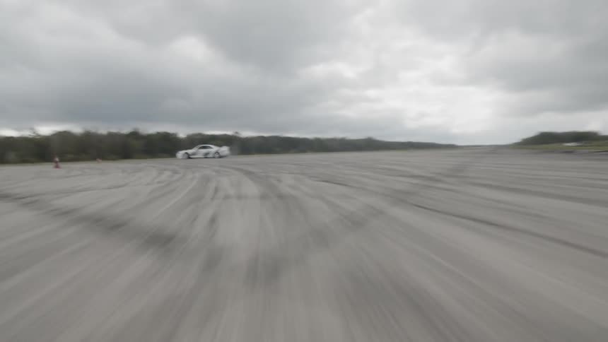 A race car drifts while speeding over a road on a cloudy day