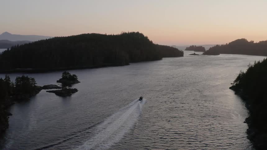 A boat motors upstream at sunset amidst a wooded and hilly land surrounding the water
