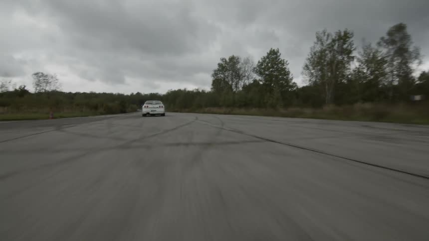 A white race car speeds over a paved road on a cloudy day