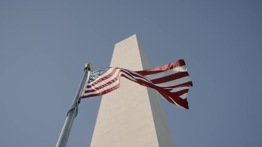 The us flag waves below a tall stone monument