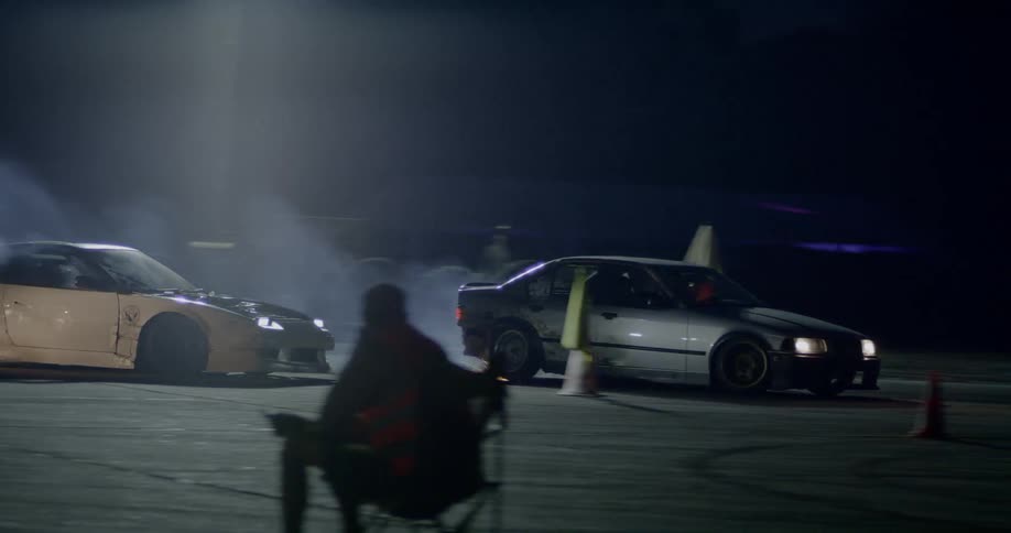 Two stock cars drift around the corner of a circuit at night