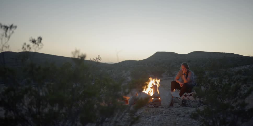 A woman sitting in a camping chair next to a campfire