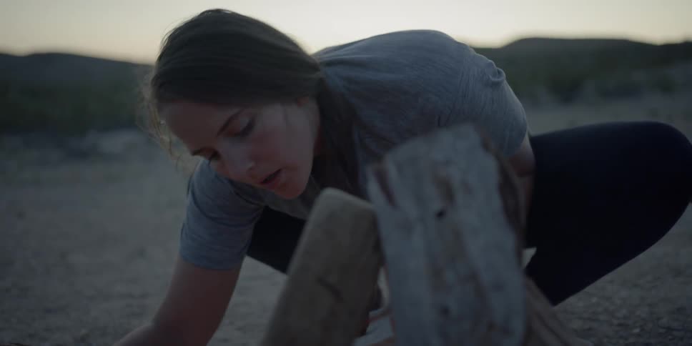 A woman is blowing on a small campfire to get it to spark larger