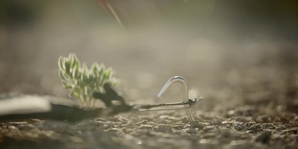 A person uses a rock to hit a tent peg into the arid ground