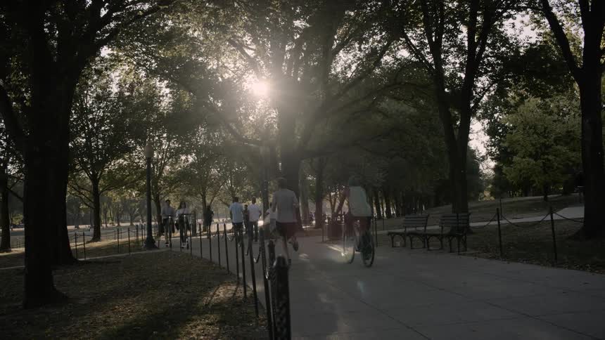 People run and cycle while woman and girl drive electric scooters in the public park