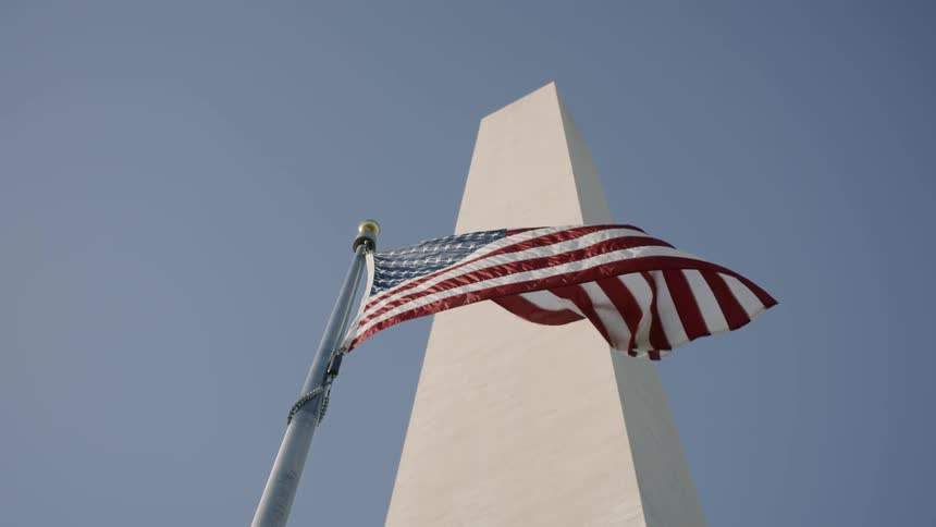 An american flag waves in the wind in front of a monument