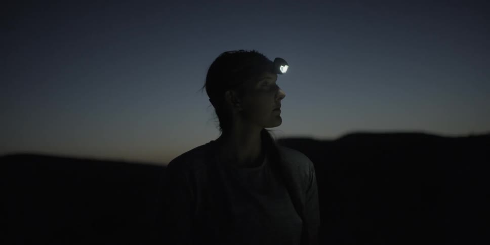 Woman wearing a headlamp stands outdoors at dusk