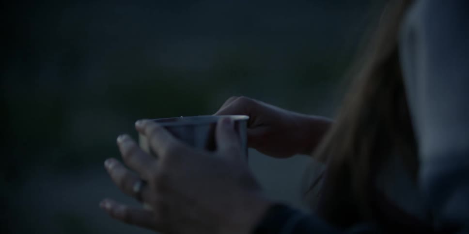 A woman stands outside at night tapping her hand on a stainless steel mug