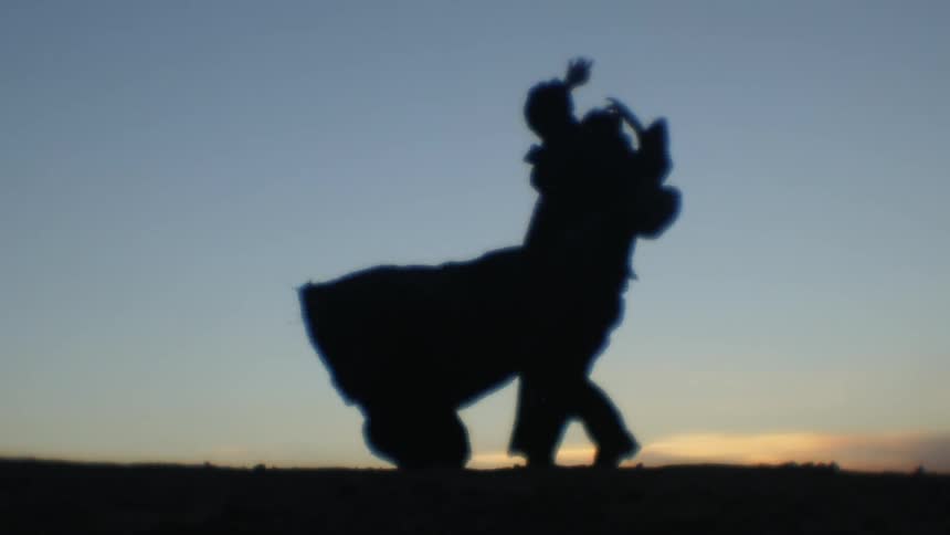 A man on top of a hill dancing in the wind at low sun while wearing a cape