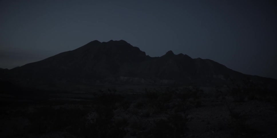 A mountain at night as moonlight outlines an arid landscape