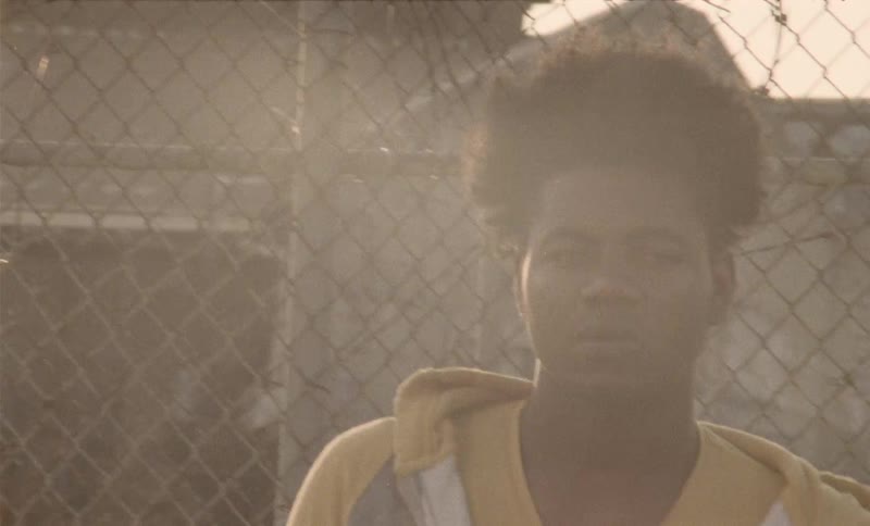 A young black male standing outside next to a fence