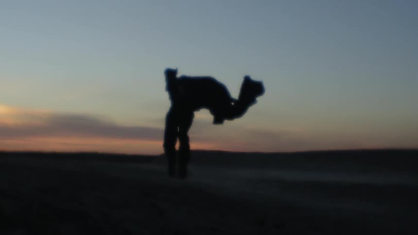 The silhouette of a man with a cape dancing and twirling in the wind at sunset