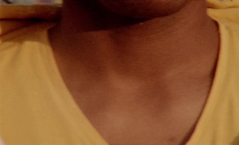 A black man wearing a yellow and brown sweatshirt leans on a chain link fence
