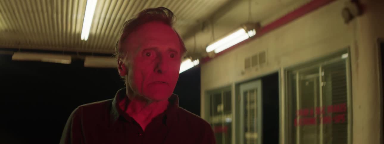 A red light and then a white light is shone in the face of a man under illuminated shelter outside of a single storey building