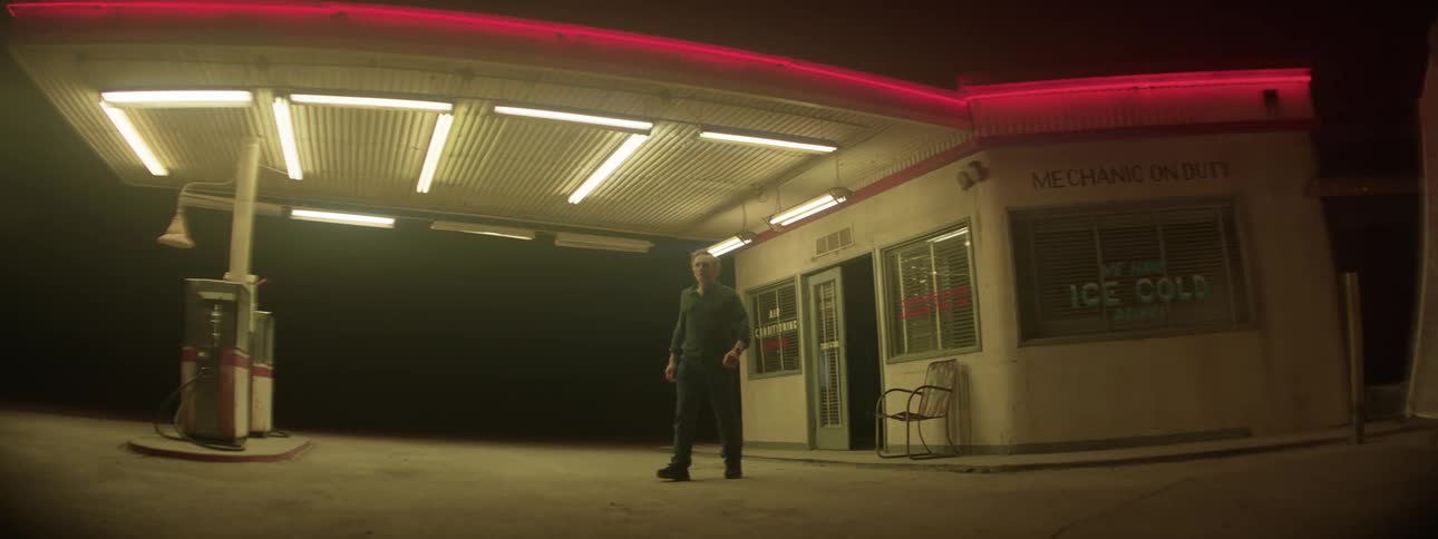 Man walks out of gas station door and walks at night
