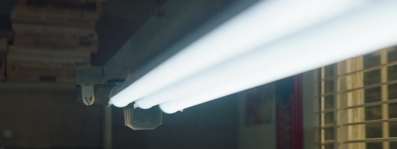 Two bulbs in a three bulb fluorescent strip light flicker by a window at night