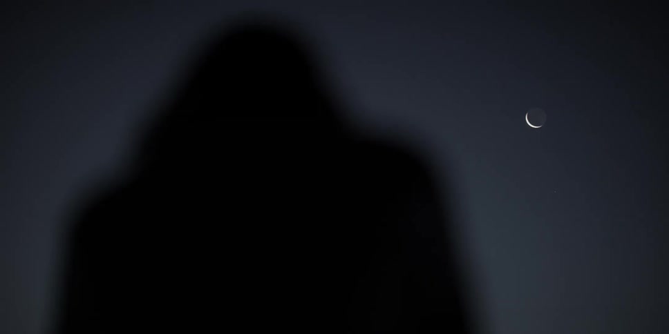 A silhouetted person looks up at the moon in a dark night sky