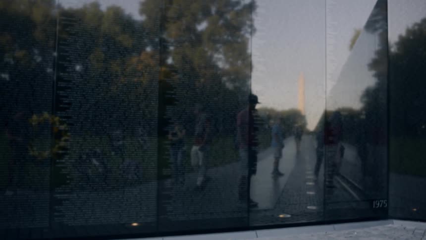 The sun reflecting off of the vietnam war monument in washington dc to reveal visitors and the washington monument in the distance