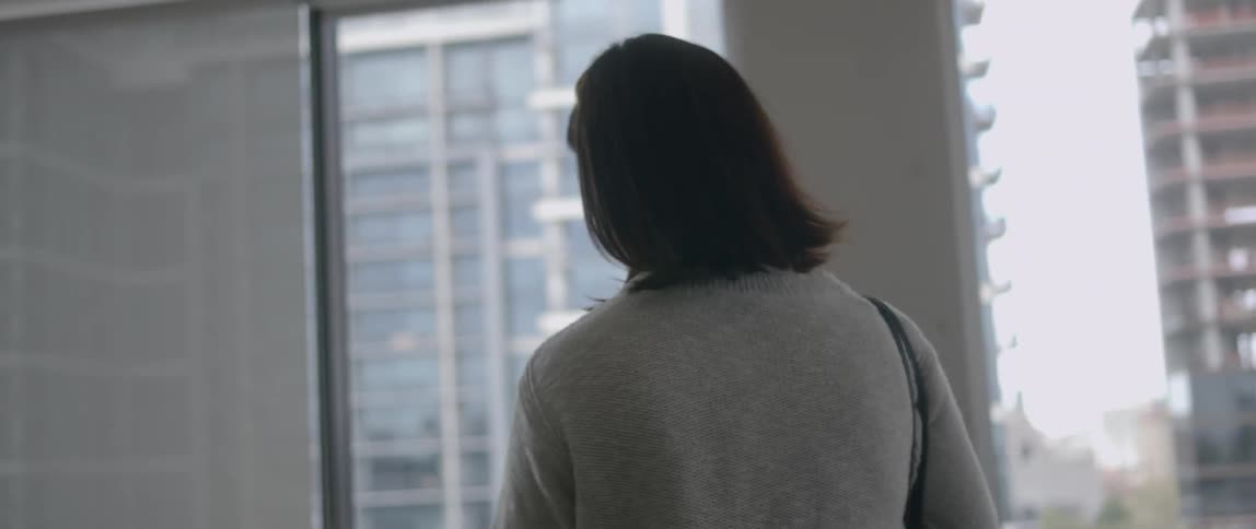 A white woman walks through an office and sits down in a desk chair