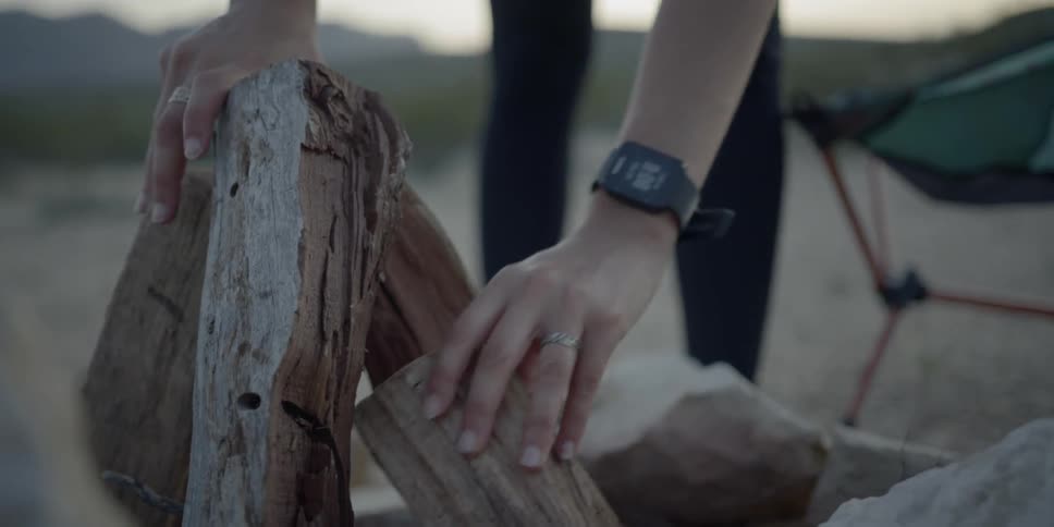 A white woman stacks logs to build a campfire