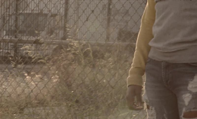 A black teenager stands in front of a fence
