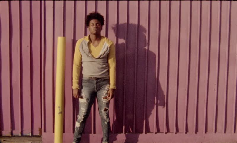 A black teenager stand next to a yellow pole