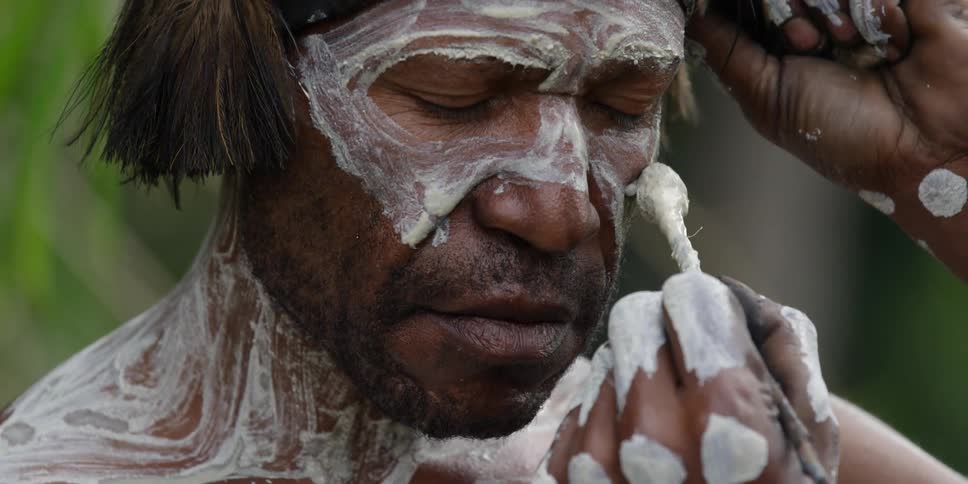 A man applying white paint to another man's face